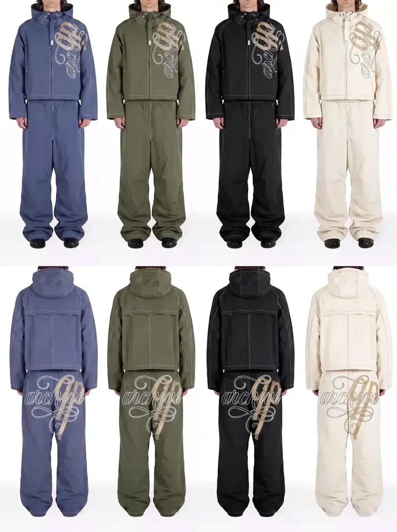 Front and back views of a hooded tracksuit with white stitching and a large script graphic, shown in four colours: blue-grey, olive, black and cream. Studio photo on a light background, heads cropped out.